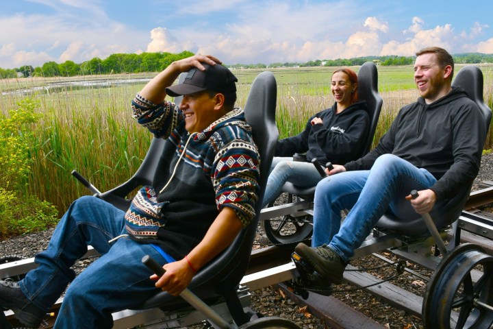 Three people riding on rail bikes through a scenic landscape.