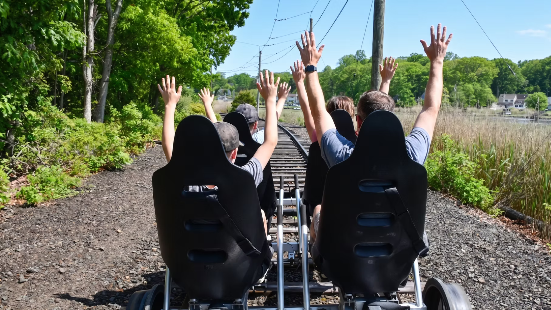 People with raised hands riding a rail bike on tracks.