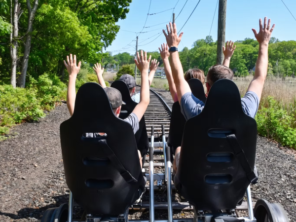 People with raised hands riding a rail bike on tracks.