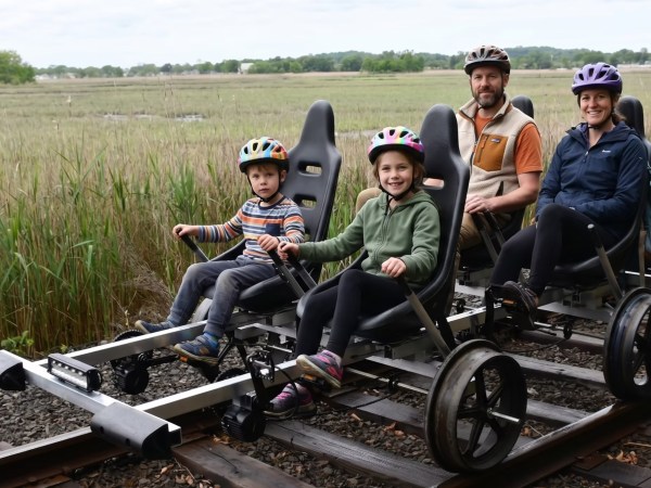 Two adults and two kids ride a quad bike on railroad tracks through a grassy landscape.